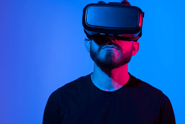 Bearded man using VR headset helmet to interacts with metaverse using swipe and stretching gestures. Watching virtual reality 3d video. Man in VR goggles looking around. - Photo, image