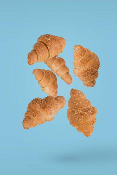Frissen sült croissant repül a levegőben elszigetelt egy fényes kék háttér. Kreatív reggeli élelmiszer koncepció. - Fotó, kép