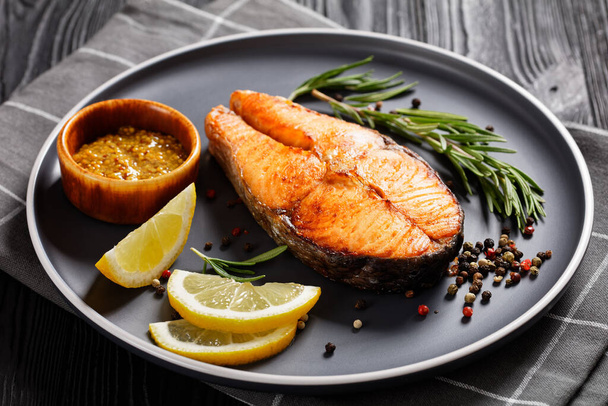 delicious baked salmon steak with wholegrain mustard, lemon, rosemary on a plate, horizontal view from above - Fotoğraf, Görsel