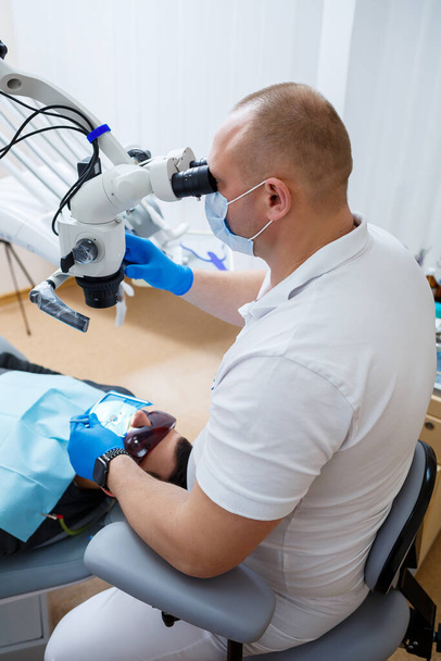 Дантист лечит зубы пациента микроскопом. Дантист лечит рот пациента. Стоматологическая помощь. Высокое качество фото - Фото, изображение