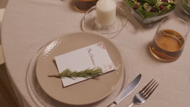 Seguimiento cercano de la mesa de la cena fijada para Navidad. La placa está decorada con tarjeta de Navidad y una pequeña rama de abeto - Metraje, vídeo