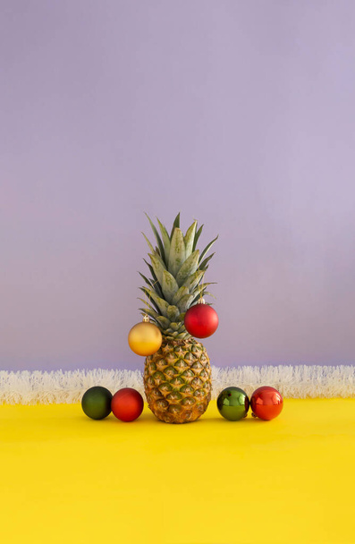 Pineapple decorated as christmas tree with white, red, green and golden baubles on vivid yelow and pastel purple background. Creative christmas celebration concept. Close up perspective. - Photo, Image