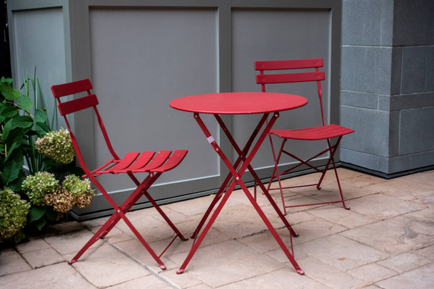 Vista isolata di due sedie rosse a un tavolo rosso all'aperto su un patio in mattoni di cemento, con lussureggiante fogliame verde sullo sfondo - Foto, immagini