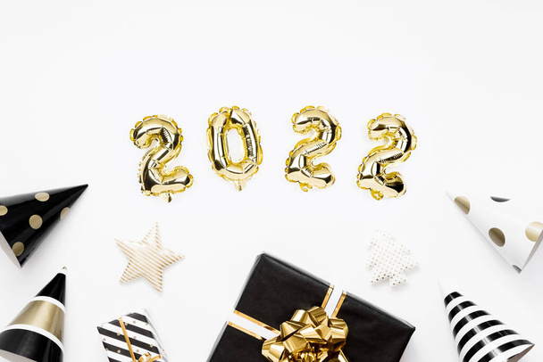Happy New year 2022 celebration card. Gold foil balloons numeral 2022 on white background. Gifts and party hats. - Foto, Imagen