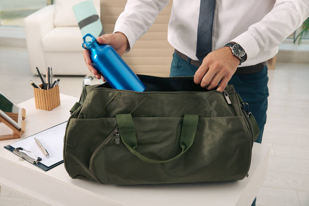 Businessman packing sports stuff for training into bag in office, closeup - Foto, imagen