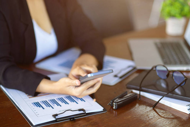 Oříznutý obrázek ženy finanční asistentky pomocí smartphonu na jejím stole v kanceláři. - Fotografie, Obrázek