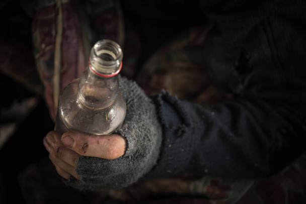 Caucásico sin hogar hombres usando guantes sin dedos con una botella de vodka de cerca. - Foto, Imagen