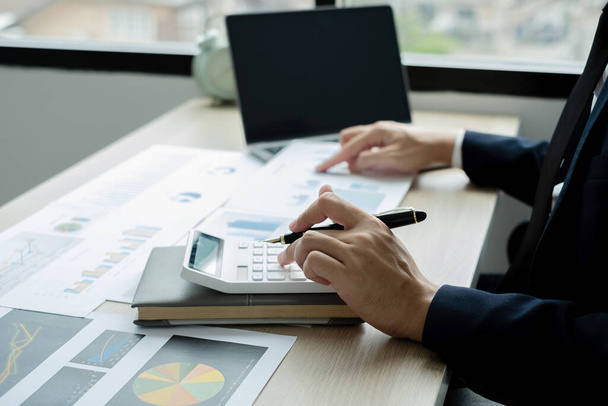 Die Hand der Geschäftsleute sitzt an ihrem Schreibtisch und berechnet Finanzgrafiken, die die Ergebnisse ihrer Investitionen zeigen, und plant einen erfolgreichen Geschäftsprozess. - Foto, Bild