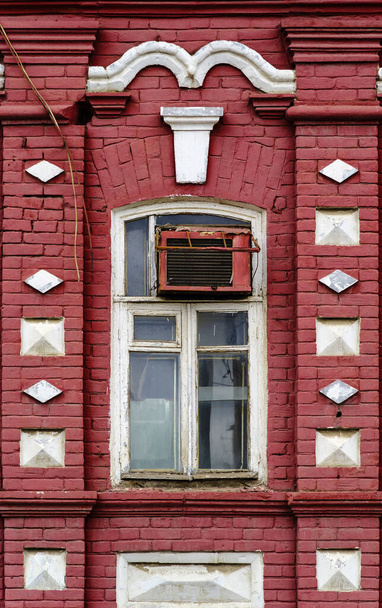 Fragment van de gevel van een oud bakstenen gebouw met een wit houten raam en airconditioning. De foto is genomen in Rusland, in de stad Orenburg - Foto, afbeelding