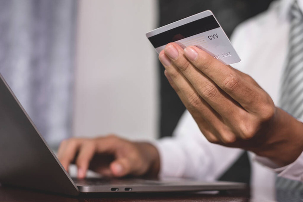 Biznesmen trzyma w ręku kartę kredytową i używa laptopa do zakupów internetowych i płatności internetowych. - Zdjęcie, obraz