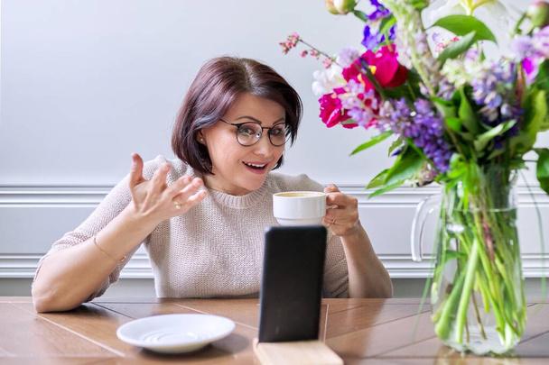 Middle-aged woman sitting at home using smartphone for video call - Фото, зображення