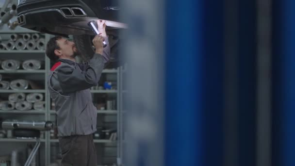 Der Mechaniker inspiziert im Autoservice die Auspuffanlage des Autos. Auto auf dem Aufzug Inspektion und Diagnose von Problemen mit der Federung des Autos - Filmmaterial, Video