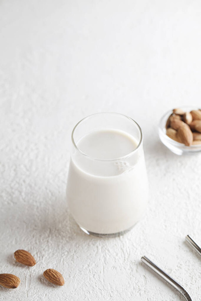 Веганське мигдальне молоко в склянці з горіхами на білому тлі. Копіювати простір. Здорова вегетаріанська їжа
.  - Фото, зображення
