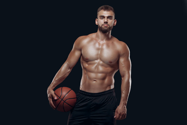 Portrait of a very muscular naked man playing basketball isolated on black background - Foto, afbeelding