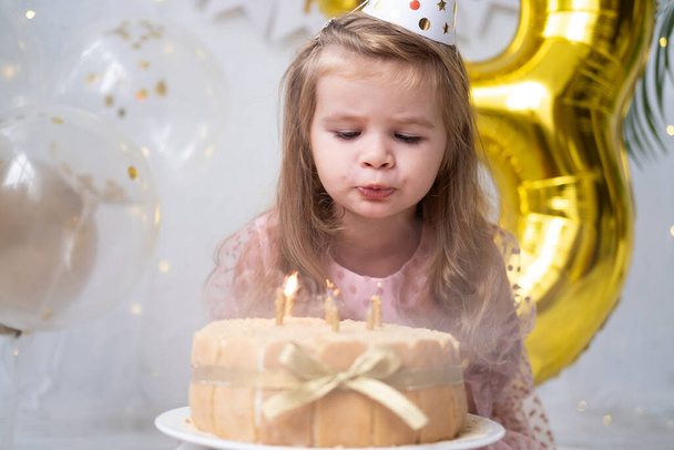 cute little child girl blowing candles on birthday cake and celebrating birthday - Photo, Image