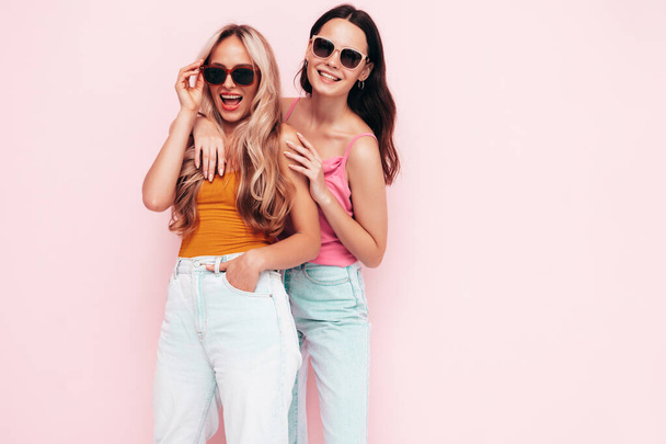 Two young beautiful smiling brunette hipster female in trendy summer clothes. Sexy carefree women posing near pink wall. Positive models having fun. Cheerful and happy. In sunglasses - Foto, afbeelding