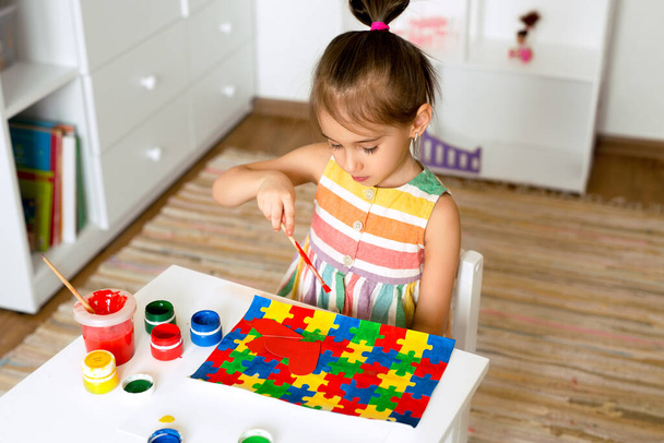 Menina desenha um desenho guache com quebra-cabeças coloridos na mesa em apoio de um amigo com síndrome do autismo. Conceito Dia Mundial da Consciência do Autismo. - Foto, Imagem