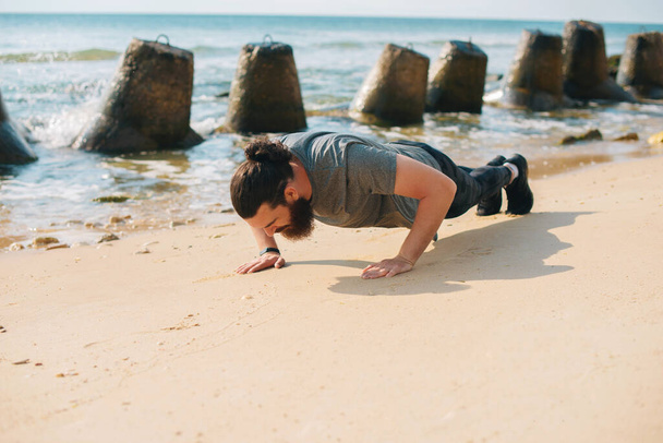 Φωτογραφία του νεαρού αθλητή που κάνει πους απς στην παραλία κοντά στη θάλασσα - Φωτογραφία, εικόνα