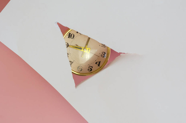 Heure 9 heures. Une horloge vintage à travers un trou dans le papier blanc sur fond rose. Horloge de table mécanique ronde en cadre doré. Concentration sélective. - Photo, image