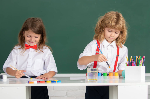 School children drawing a colorful pictures with pencil crayons in classroom on blackboard background. Portrait of cute pupils enjoying art and craft lesson. - Foto, Imagem