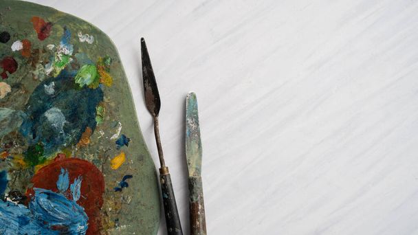 Close-up van het kunstenaarspalet bedekt met verf met paletmessen en kopieerruimte - Foto, afbeelding