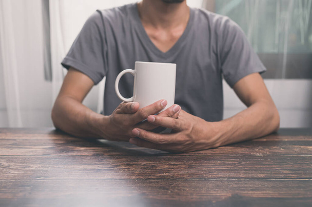 A male holding a white mug sitting at the table - Foto, Imagem
