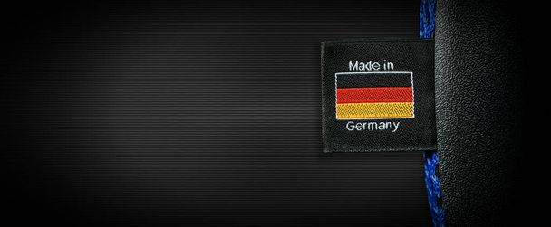 Etykieta z flagą niemiecką i tekstem Made in Germany przyszyta do czarnej tkaniny, na czarnym tle z przestrzenią do kopiowania. - Zdjęcie, obraz