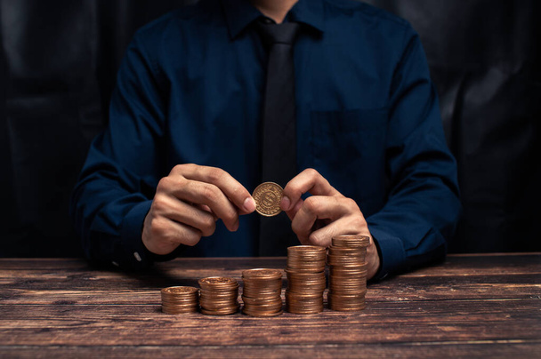 A businessman with stacking coins on a wooden table - Foto, afbeelding
