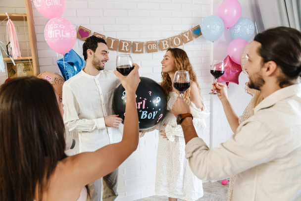 Happy young pregnant woman with friends at a baby shower, poping gender balloon - Фото, изображение