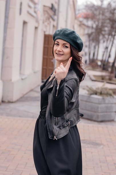 A portrait of a smiling girl in a leather jacket, a long black dress with a beret on her head, posing on the streets of the city. Style and fashion concept. Happy smiling girl. - Photo, image