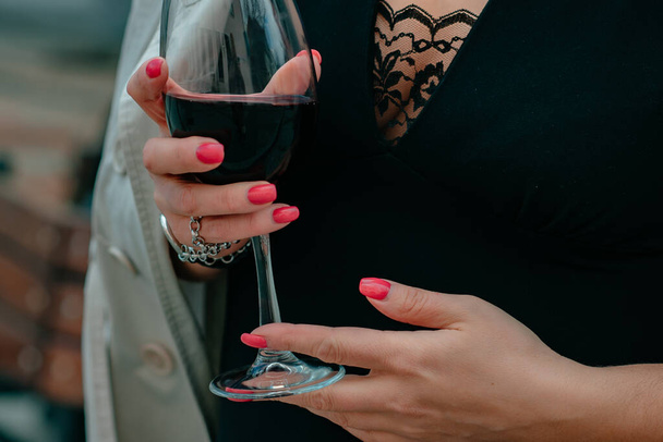 Close-up photo, a girl holding a glass of red wine in her hands, a woman with a red manicure. - Zdjęcie, obraz