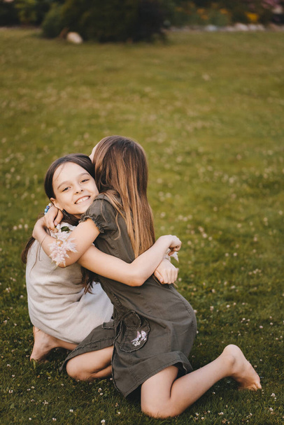Portrait of two little girls in delicate dresses hugging each other outdoors. Friends are having fun together in the fresh air. Beautiful delicate bouquet of flowers in the hands of a child. - Foto, Imagem