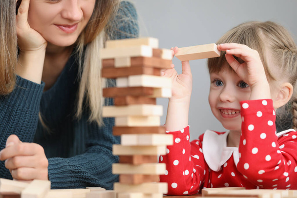 mooi klein kind trekken houten blok uit toren en glimlach - Foto, afbeelding