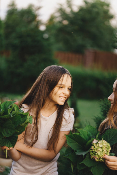 Portrait of two little girls who are walking in the park,picking flowers.Beautiful delicate bouquet of flowers in the hands of a child.White hydrangea.Friends are having fun together in the fresh air. - Zdjęcie, obraz