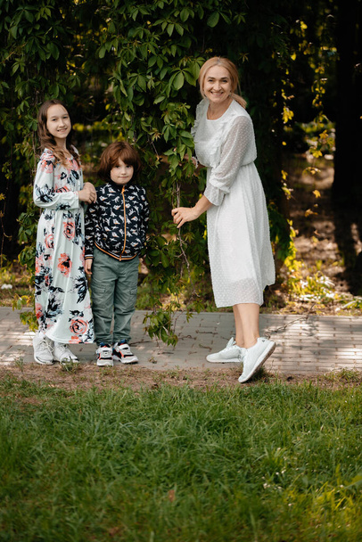 A smiling mother with her daughter and son are walking in the botanical garden among climbing plants. Mom and daughter in delicate summer dresses are walking in the park, spending time together, with their family. - Foto, Imagem