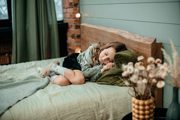 A little girl sleeps cute on a large bed in a cozy room, next to a vase with decorative flowers. The child sleeps in bed. Rest and relaxation concept. - Valokuva, kuva