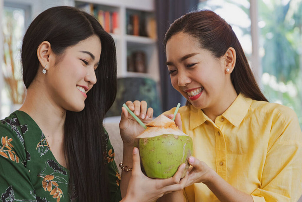 Retrato de dos amigos asiáticos de pelo largo bebiendo agua dulce de coco juntos, fruta orgánica: Felicidad en la casa, jugos de frutas naturales, los dos compiten por bebidas con sonrisas - Foto, imagen