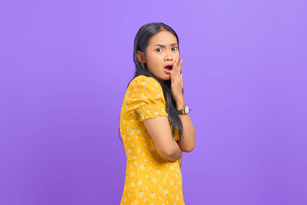 Choqué jeune femme asiatique levé une main et écouter de bonnes nouvelles sur fond violet - Photo, image