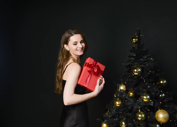 Beautiful young woman at the Christmas tree. An elegant woman. - Фото, зображення