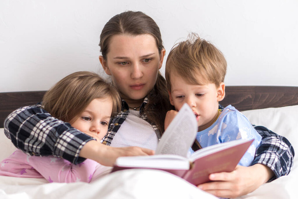 happy family. Close up loving mother lying with daughter son two kids pajamas in bed children reading interesting storybook, preschool smiling kid girl enjoy fairytale before go to sleep good pastime - Φωτογραφία, εικόνα