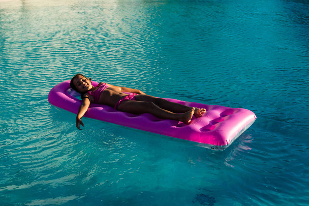little girl floats on an inflatable mattress in the pool - Photo, Image