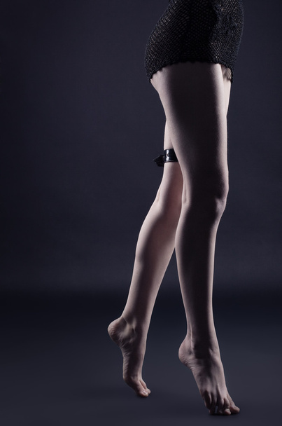 Woman legs in dark with leather strap - Foto, afbeelding