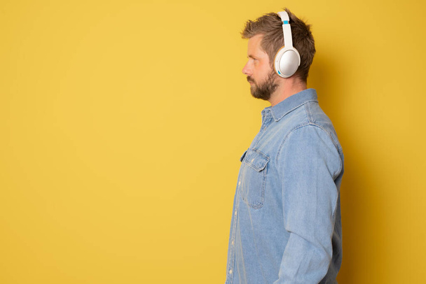 Profile portrait young man in headphones standing isolated over yellow background. - Photo, Image