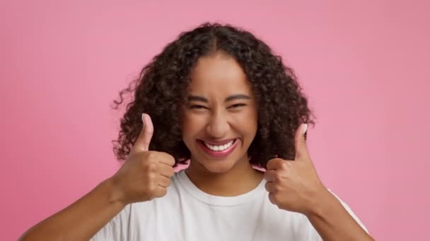 Mujer negra gestos pulgares hacia arriba con ambas manos, fondo rosa - Metraje, vídeo