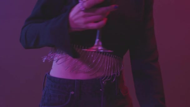 Midsectie slowmo schot van onherkenbare jonge vrouw in fancy lange mouw gewas top dansen op neon feest met vrienden klinkende rode wijn glazen en bier fles - Video