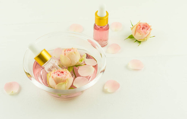 cosmetic rose oil in bottles with a pipette in a glass bowl on a white wooden table. the concept of natural self-care - Fotografie, Obrázek
