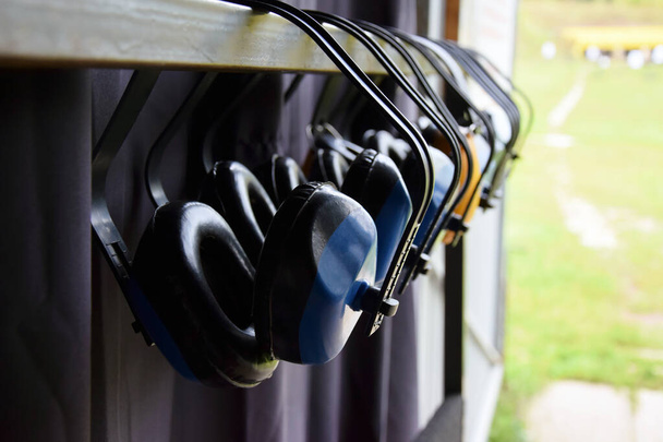 Muchos audífonos deportivos de tiro cuelgan de una percha en el campo de tiro. Protección del oído. - Foto, imagen