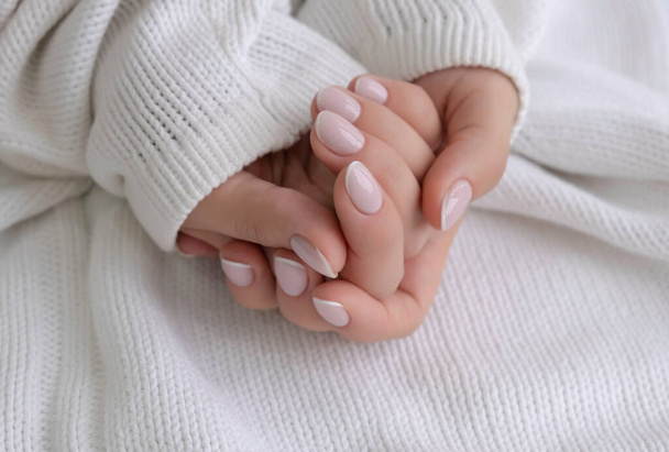 Well-groomed female hands, delicate manicure on a white knitted background, close-up - 写真・画像