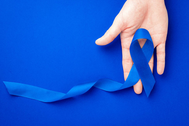 Los hombres cáncer. Cinta azul en manos aisladas sobre fondo azul profundo. Concienciación sobre el cáncer de próstata de los hombres salud en noviembre. Concepto de carcinoma suprarrenal - Foto, Imagen