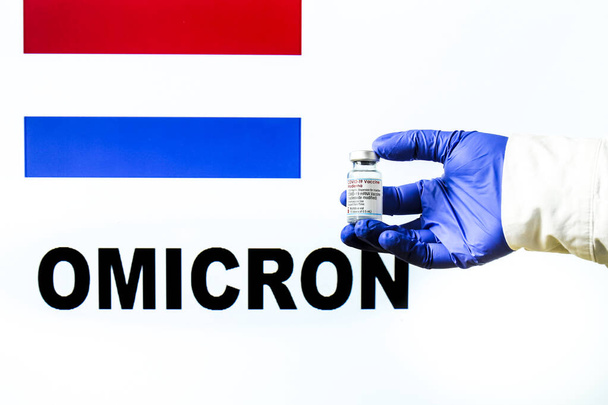 Madrid, Spanyolország - 2021. november 29.: Kézben tartó injekciós üveg Moderna covid vakcinával. Holland zászló és Omicron kovid változat szó írva a háttérben - Fotó, kép